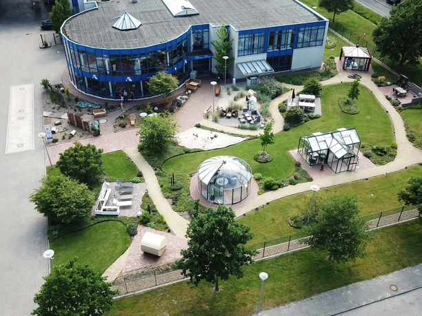 Aussenanlage dekoVries Die Außenanlage dekoVries zeigt moderne Gartenarchitektur mit geschwungenen Wegen, grünen Rasenflächen und mehreren, elegant gestalteten Pavillons.