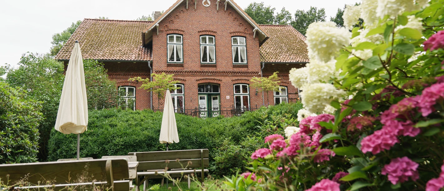 Geverdsorf - Gut Niendieck Backsteingut mit blühendem Garten, weißen und pinken Hortensien sowie Sitzplätzen im Grünen.