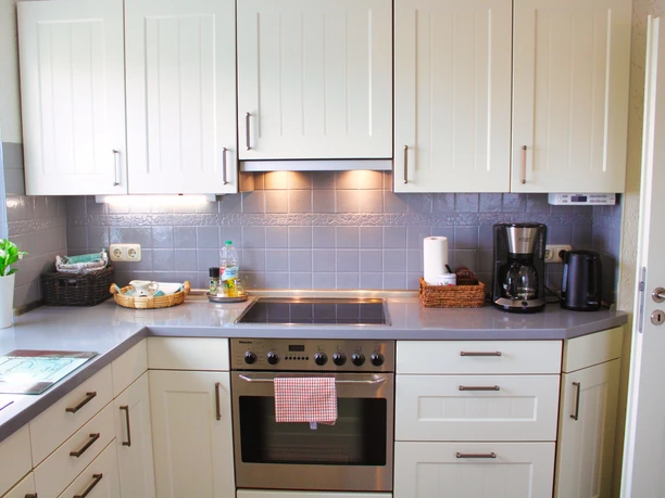 Küche Ofen Weiße Einbauküche mit grauem Fliesenspiegel, Backofen, Herd, Kaffeemaschine und Wasserkocher.