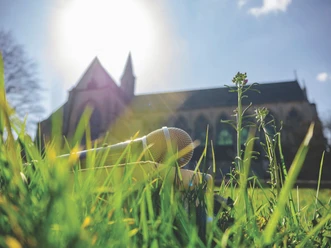 Literatur am Dom Mikrofon liegt im grünen Gras vor einer Kirche bei Sonnenschein im Hintergrund.