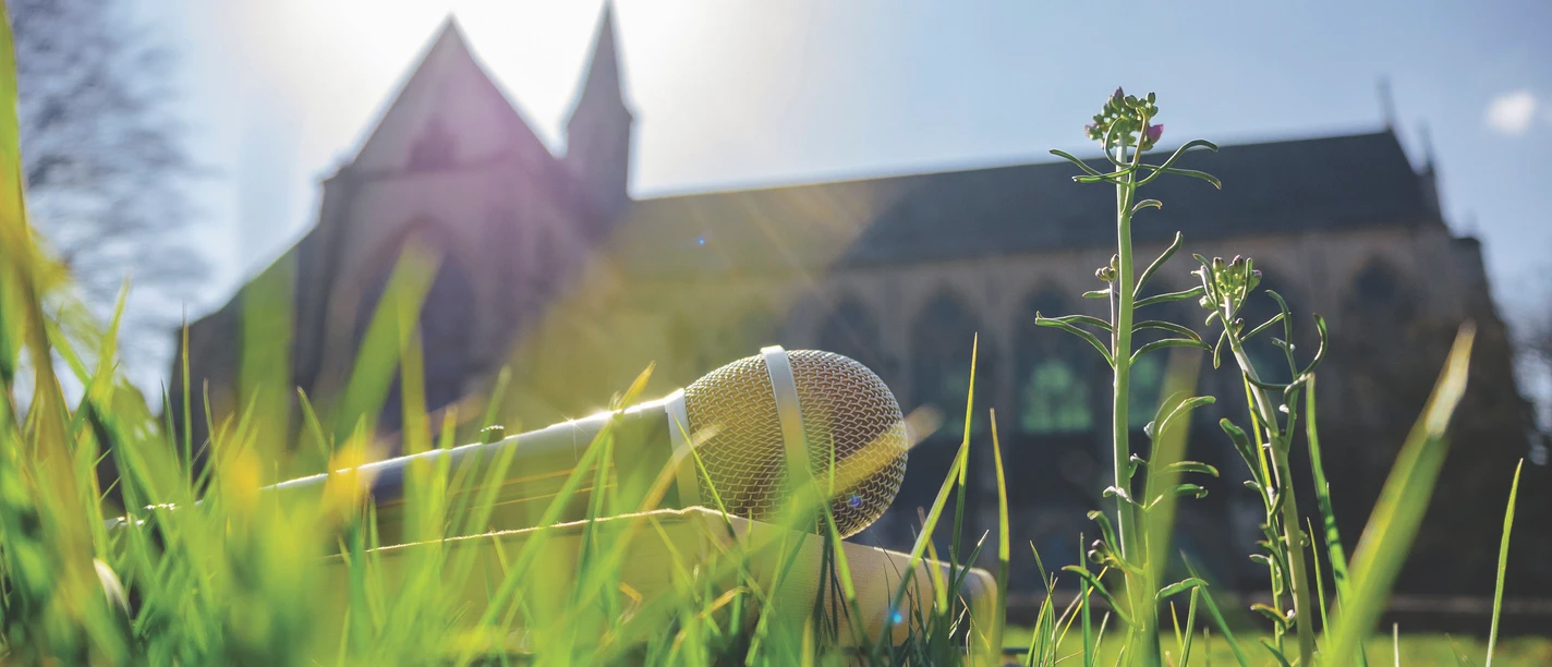 Literatur am Dom Mikrofon liegt im grünen Gras vor einer Kirche bei Sonnenschein im Hintergrund.