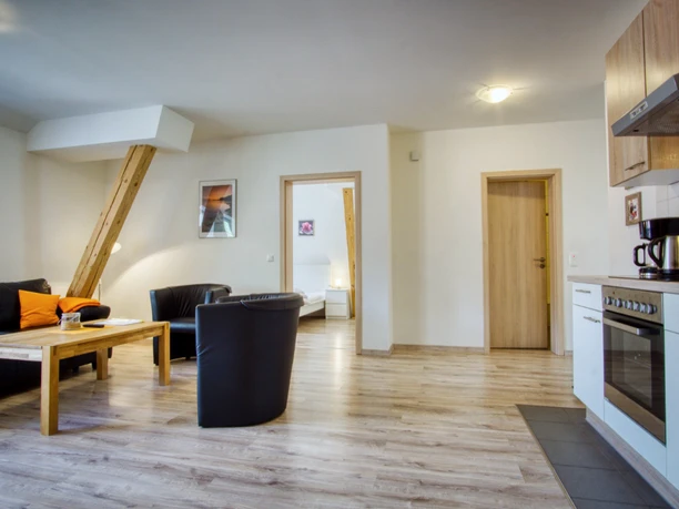 Wohnzimmer Offener Wohnraum mit Küchenzeile, schwarzen Ledermöbeln, Holztisch und Balken.