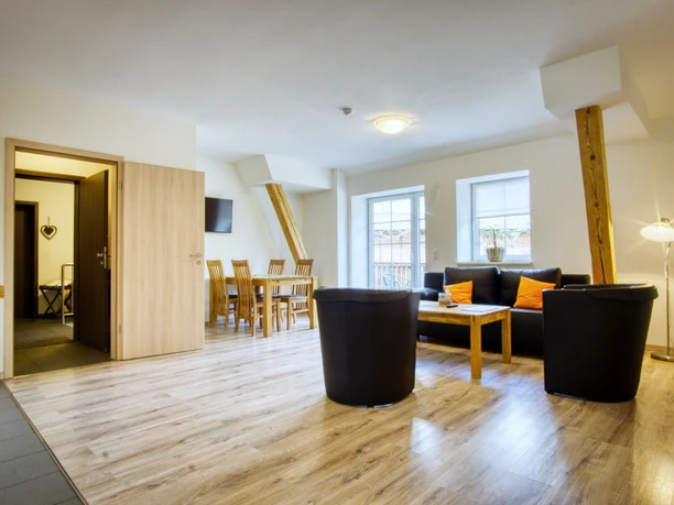 Wohn-Essbereich Heller Wohn-Essbereich mit dunklen Ledermöbeln, Holzesstisch und sichtbaren Holzbalken.