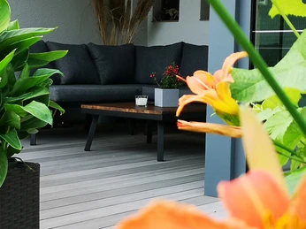 Geräumige Terrasse mit modernen Sitzmöbeln, umgeben von üppigen Pflanzen, darunter orangefarbene Blumen.