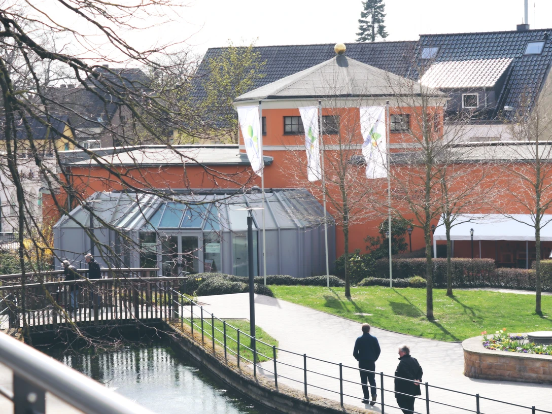IMG_0144.JPG Zwei Personen spazieren auf einem Weg entlang eines Kanals neben einem Gebäude mit oranger Fassade.