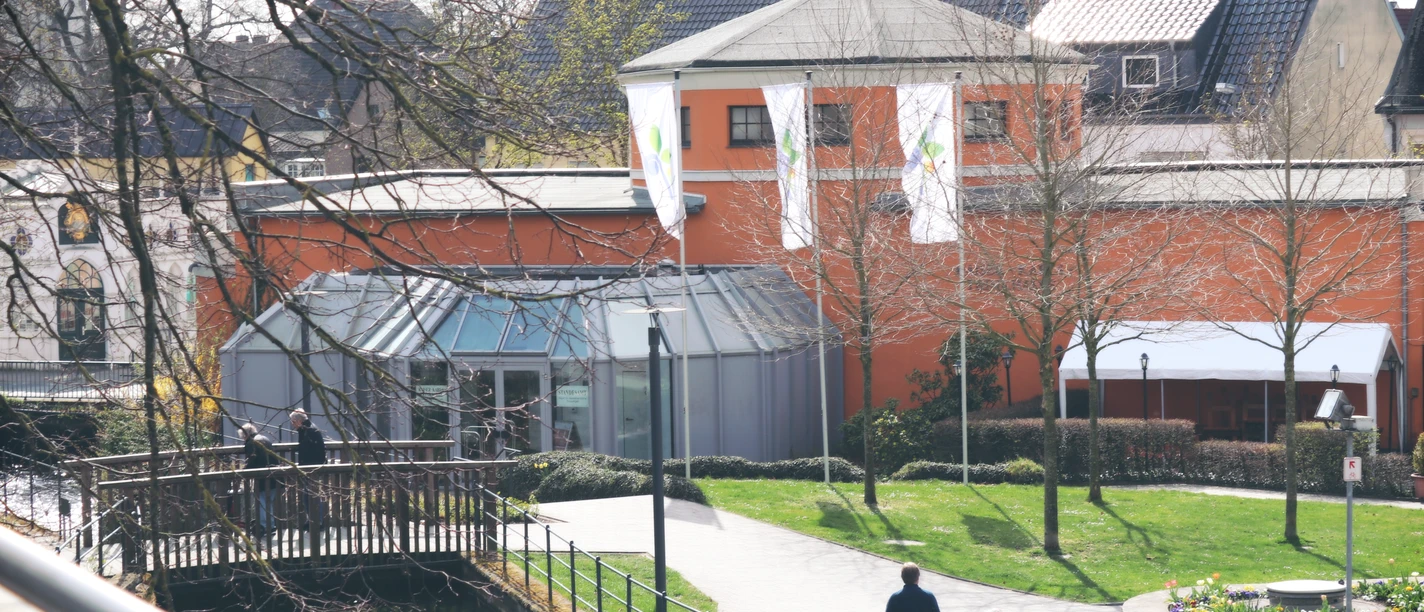 IMG_0144.JPG Zwei Personen spazieren auf einem Weg entlang eines Kanals neben einem Gebäude mit oranger Fassade.