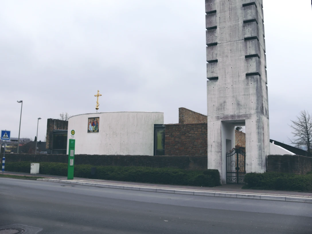 IMG_0494.JPG Kirche mit modernem Turm, umgeben von Straßen und Bäumen unter grauem Himmel. Ruhige Umgebung im Bild.