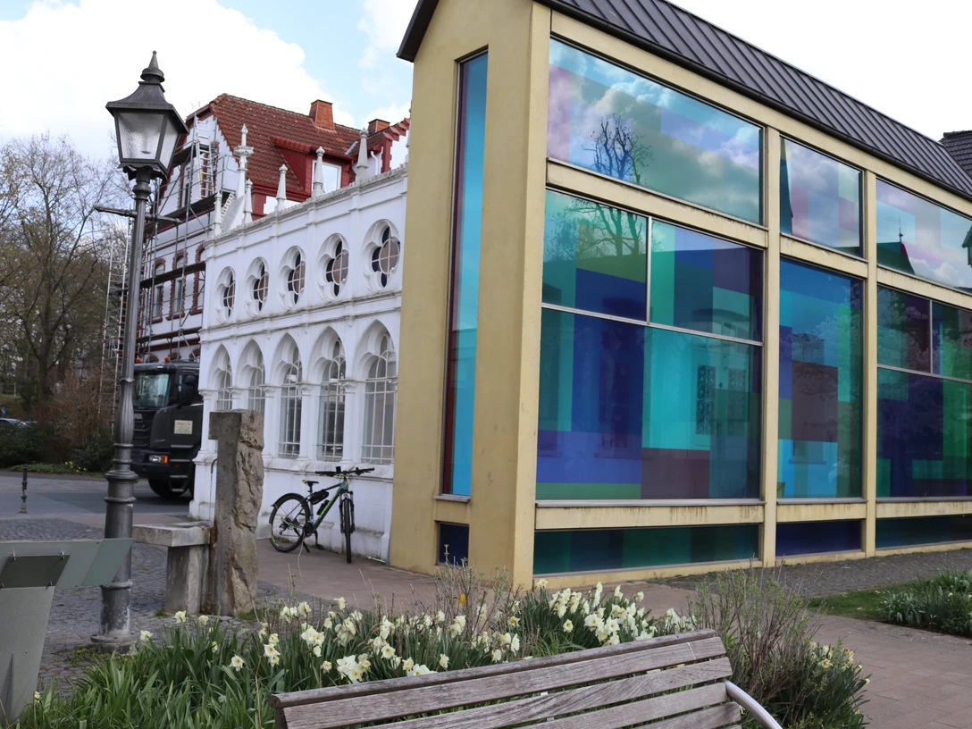 Städtische Ansicht mit modernem Gebäudeteil, bunten Glasfassaden und einer Laterne im Vordergrund.