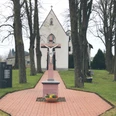 Kreuzweg mit Jesusfigur auf rotem Sockel, flankiert von hohen Bäumen, führt zur Kapelle im Hintergrund.