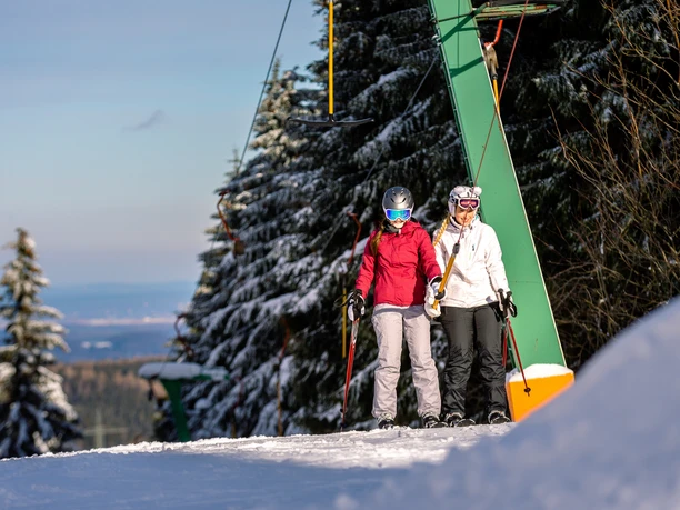 Two skiers on a sunny day on a snowy slope near a ski lift.