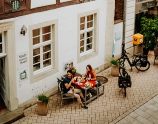 Zwei Personen genießen ein Essen im Freien vor einem historischen Fachwerkgebäude in Brakel.