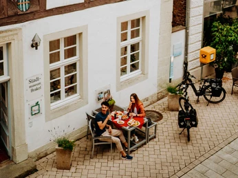 Zwei Personen genießen ein Essen im Freien vor einem historischen Fachwerkgebäude in Brakel.