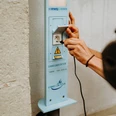 Eine Person schließt ein Ladekabel an eine E-Bike-Ladestation an einer hellen Wand an.