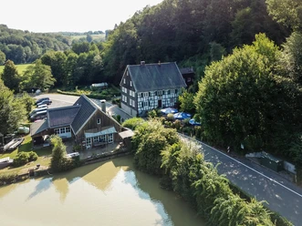 Biergarten Neuemühle <p>Fachwerkhaus und modernes Gebäude am Wasser, umgeben von Bäumen in ländlicher Umgebung.</p>