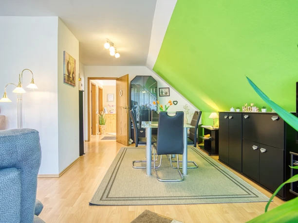 Essbereich-Pallme .jpeg Essbereich mit Glastisch, vier schwarzen Stühlen und Sideboard unter einer grünen Dachschräge.