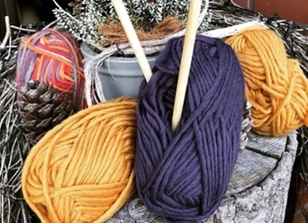 Handarbeitsgruppe.jpg Auf einem Baumstumpf liegen farbige Wollknäuel neben Stricknadeln.