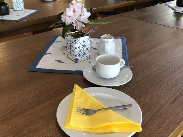 Kloencafe2.JPG Auf einem Holztisch steht ein gedeckter Tisch mit einer gelben Serviette.
