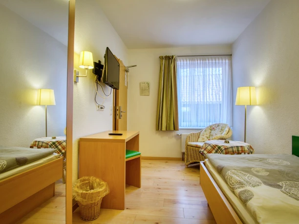 Einzelzimmer-thieshof (1).jpg Einzelzimmer mit Holzbett, Schreibtisch, Wand-TV, großem Spiegel und Korbsessel am Fenster.