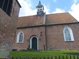 Kirche Jennelt Backsteinkirche mit rotem Ziegeldach, hohem Uhrenturm und spitzbogigen Fenstern unter blauem Himmel.