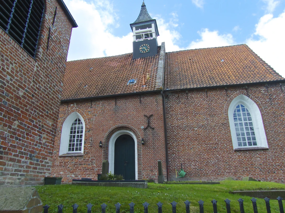 Kirche Jennelt Backsteinkirche mit rotem Ziegeldach, hohem Uhrenturm und spitzbogigen Fenstern unter blauem Himmel.