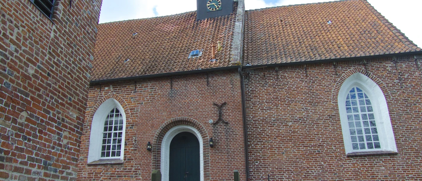 Kirche Jennelt Backsteinkirche mit rotem Ziegeldach, hohem Uhrenturm und spitzbogigen Fenstern unter blauem Himmel.