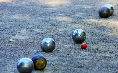 boule-bad-zwischenahn Metallene Boulekugeln liegen auf einer sandigen Spielfläche neben einer kleinen roten Zielkugel.