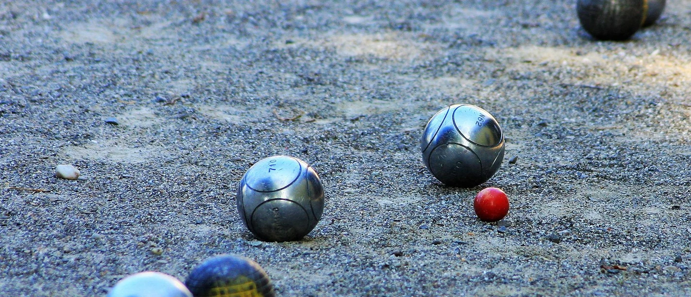boule-bad-zwischenahn Metallene Boulekugeln liegen auf einer sandigen Spielfläche neben einer kleinen roten Zielkugel.
