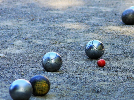 boule-bad-zwischenahn Metallene Boulekugeln liegen auf einer sandigen Spielfläche neben einer kleinen roten Zielkugel.