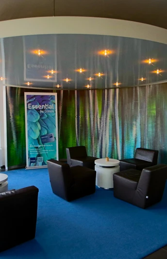 Eine moderne Rezeption mit Ledersesseln um kleine Tische auf blauem Teppichkreis, umgeben von Prospekten.