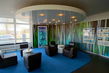 Lounge Rezeption Eine moderne Rezeption mit Ledersesseln um kleine Tische auf blauem Teppichkreis, umgeben von Prospekten.