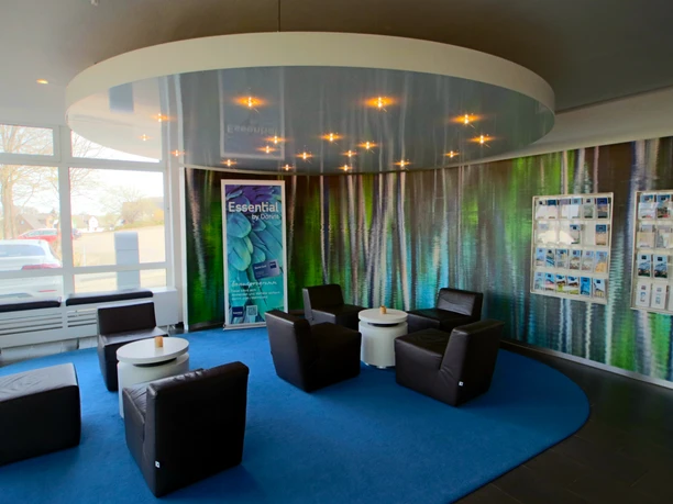 Lounge Rezeption Eine moderne Rezeption mit Ledersesseln um kleine Tische auf blauem Teppichkreis, umgeben von Prospekten.