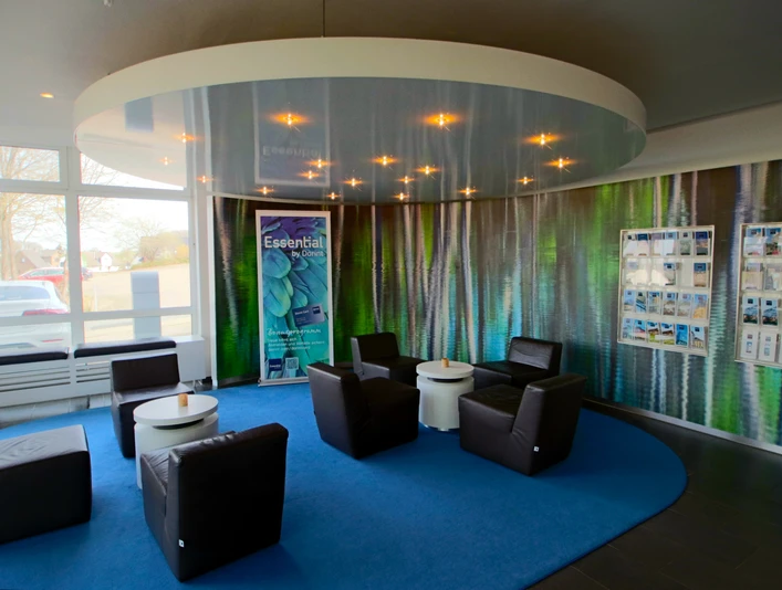 Lounge Rezeption Eine moderne Rezeption mit Ledersesseln um kleine Tische auf blauem Teppichkreis, umgeben von Prospekten.