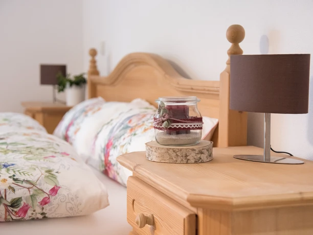 Helles Gästezimmer mit Holzbett, floraler Bettwäsche, Nachttisch, Kerze und Tischlampe