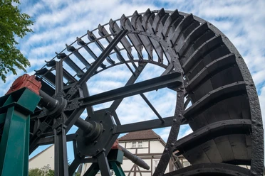 Mühlrad Altes Mühlrad aus Holz und Metall in Bewegung, vor einem Fachwerkhaus und blauem Himmel.