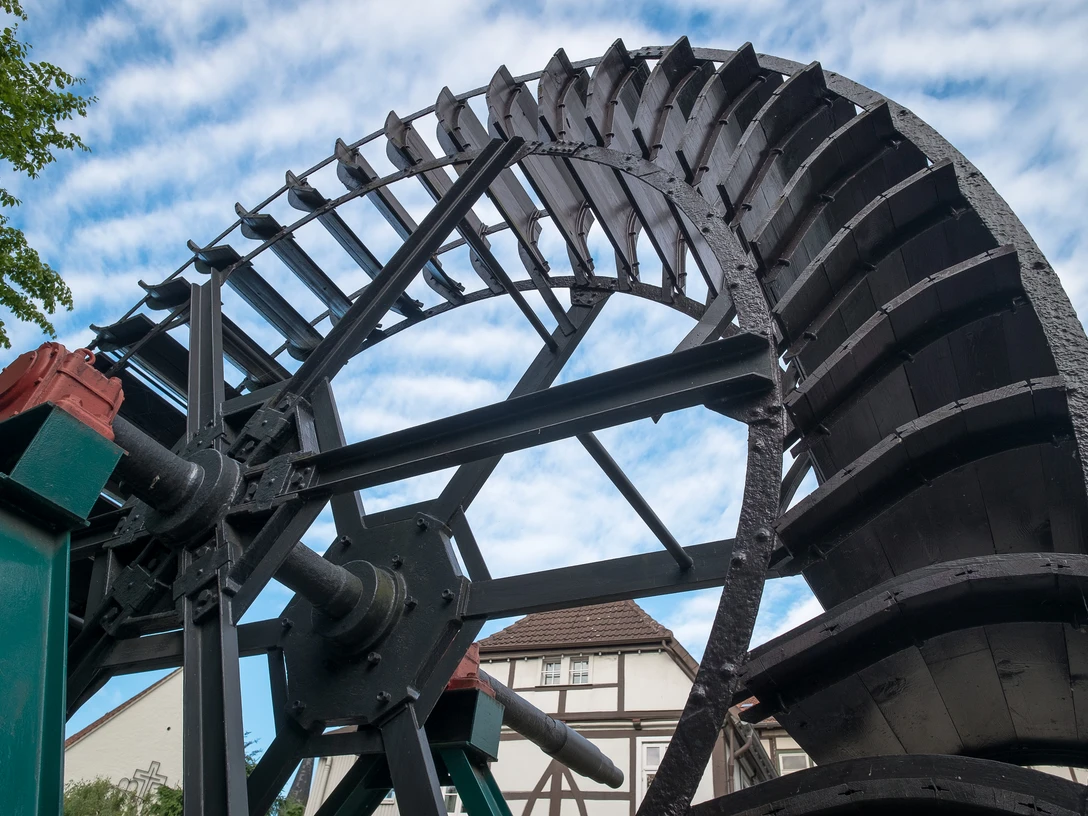Mühlrad Altes Mühlrad aus Holz und Metall in Bewegung, vor einem Fachwerkhaus und blauem Himmel.