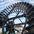 Mühlrad Altes Mühlrad aus Holz und Metall in Bewegung, vor einem Fachwerkhaus und blauem Himmel.