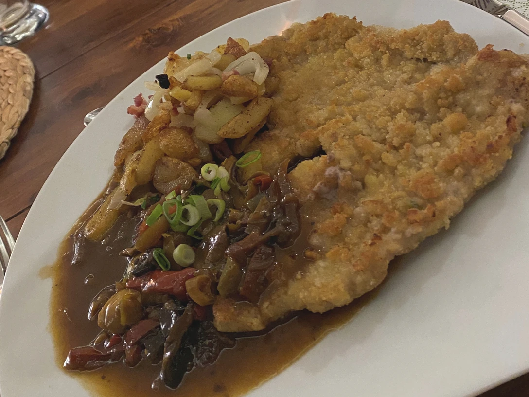 Ein golden gebackenes Jägerschnitzel auf einem weißen Teller mit Pilzsoße und gebratenen Kartoffeln.
