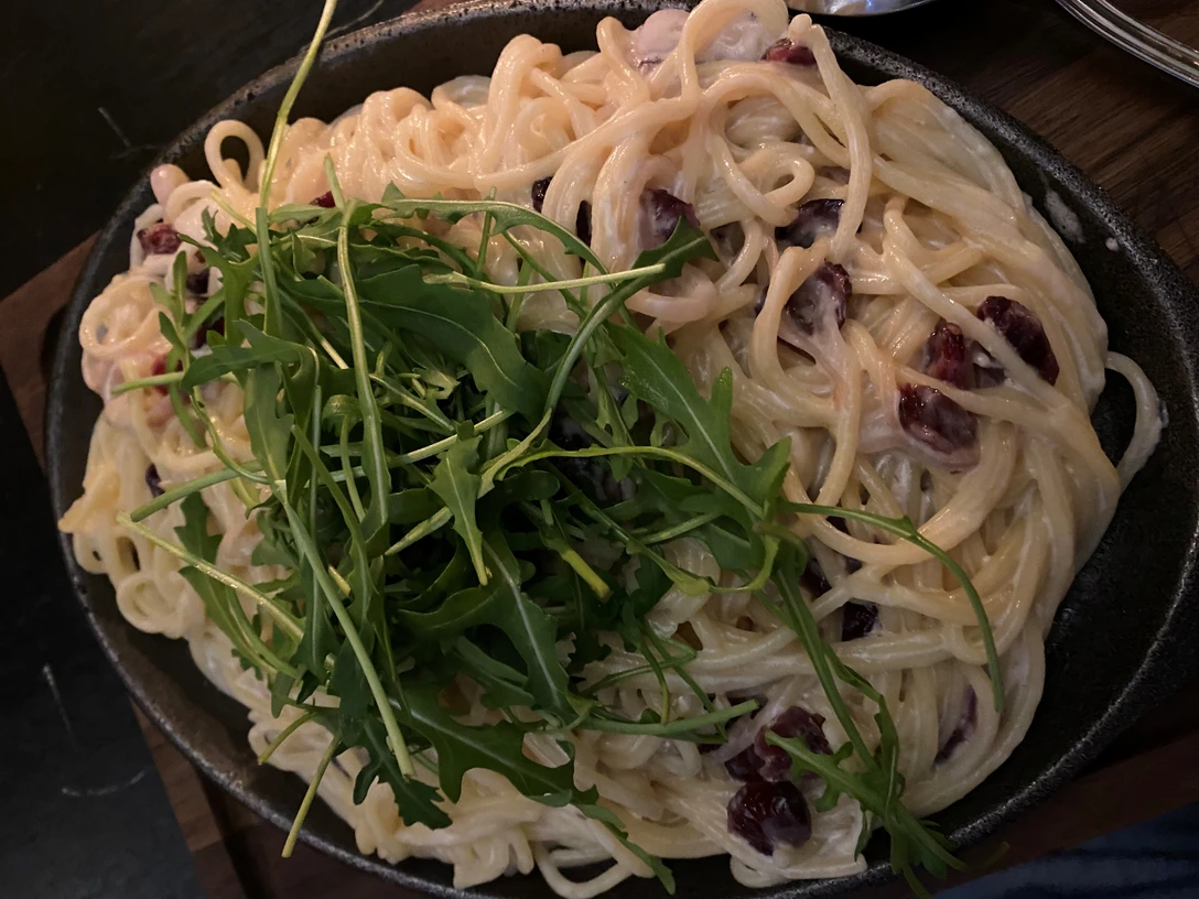 Nudelgericht Ein Teller mit Spaghetti, bedeckt mit sahniger Soße und mit frischem Rucola und Oliven garniert.