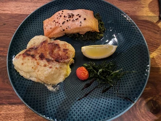 Salmon fillet on a bed of green vegetables with potato gratin, cherry tomato and lemon wedge.