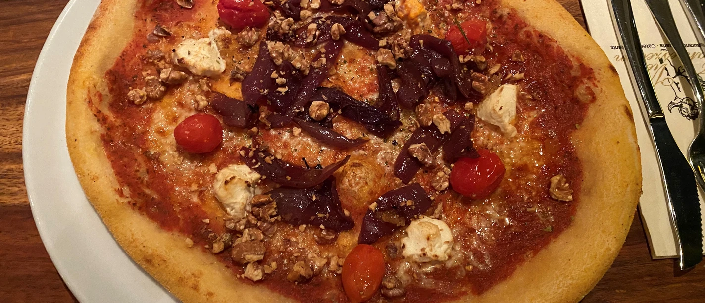 A crispy pizza with red cherry tomatoes, purple onion strips and pieces of light cheese.