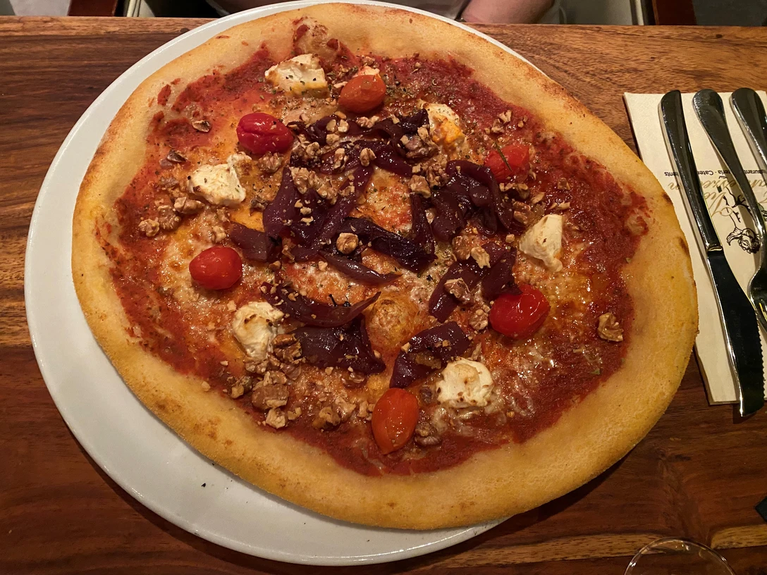 Pizza Eine knusprige Pizza mit roten Kirschtomaten, violetten Zwiebelstreifen und hellen Käsestücken.