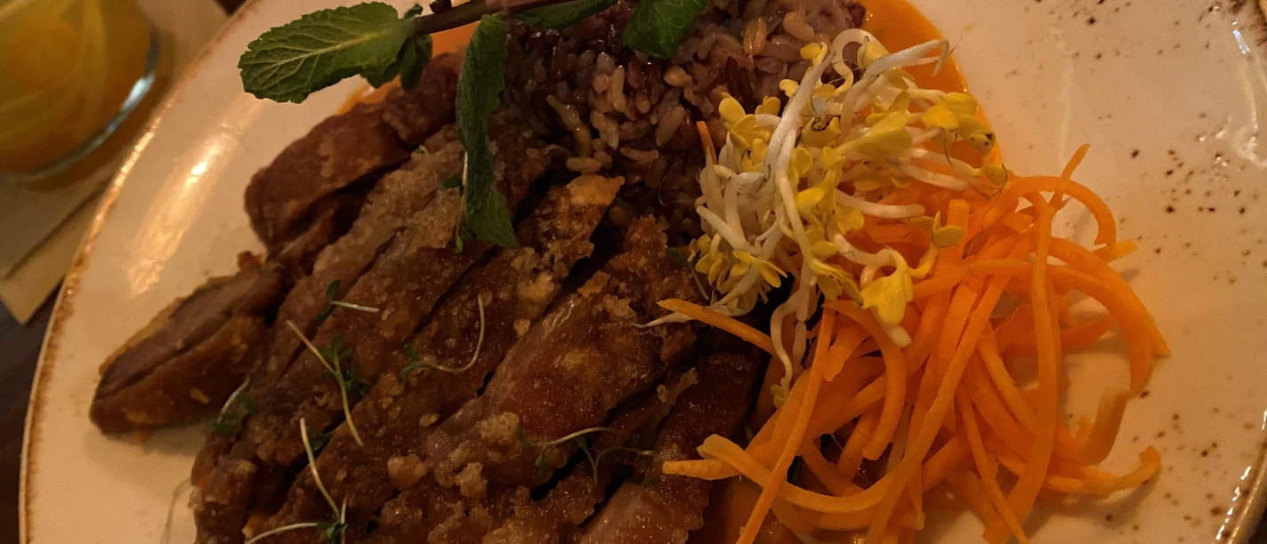 Krokante eendenborst geserveerd met rijst, groenten en muntgarnituur op een wit bord.