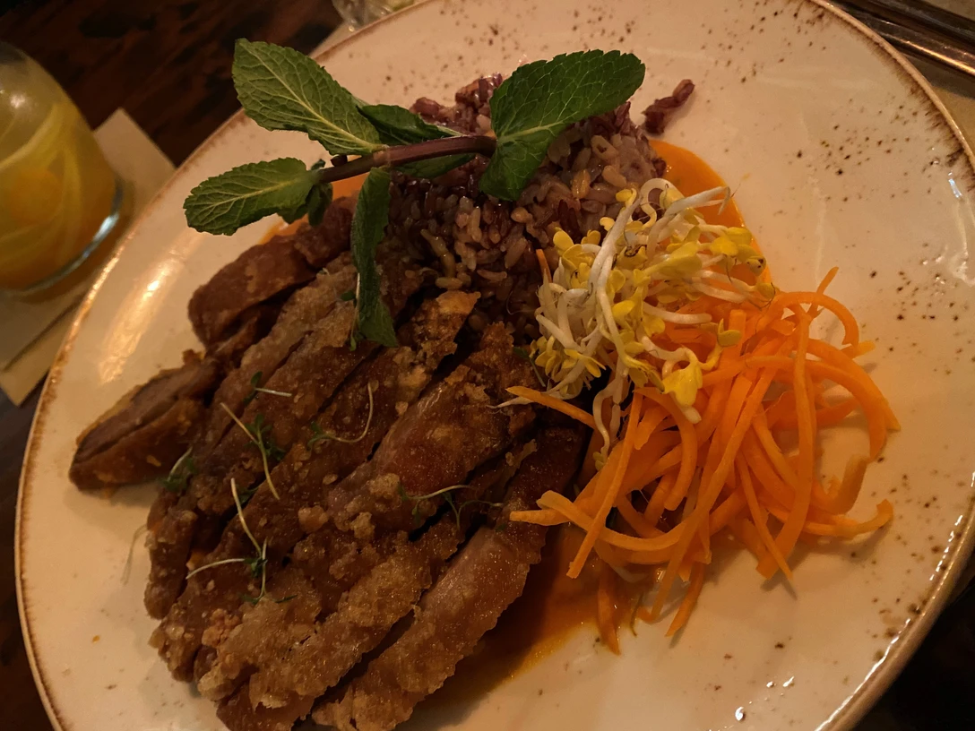 Entengericht Knusprige Entenbrust an Reis mit Gemüse und Minzgarnitur auf einem weißen Teller angerichtet.