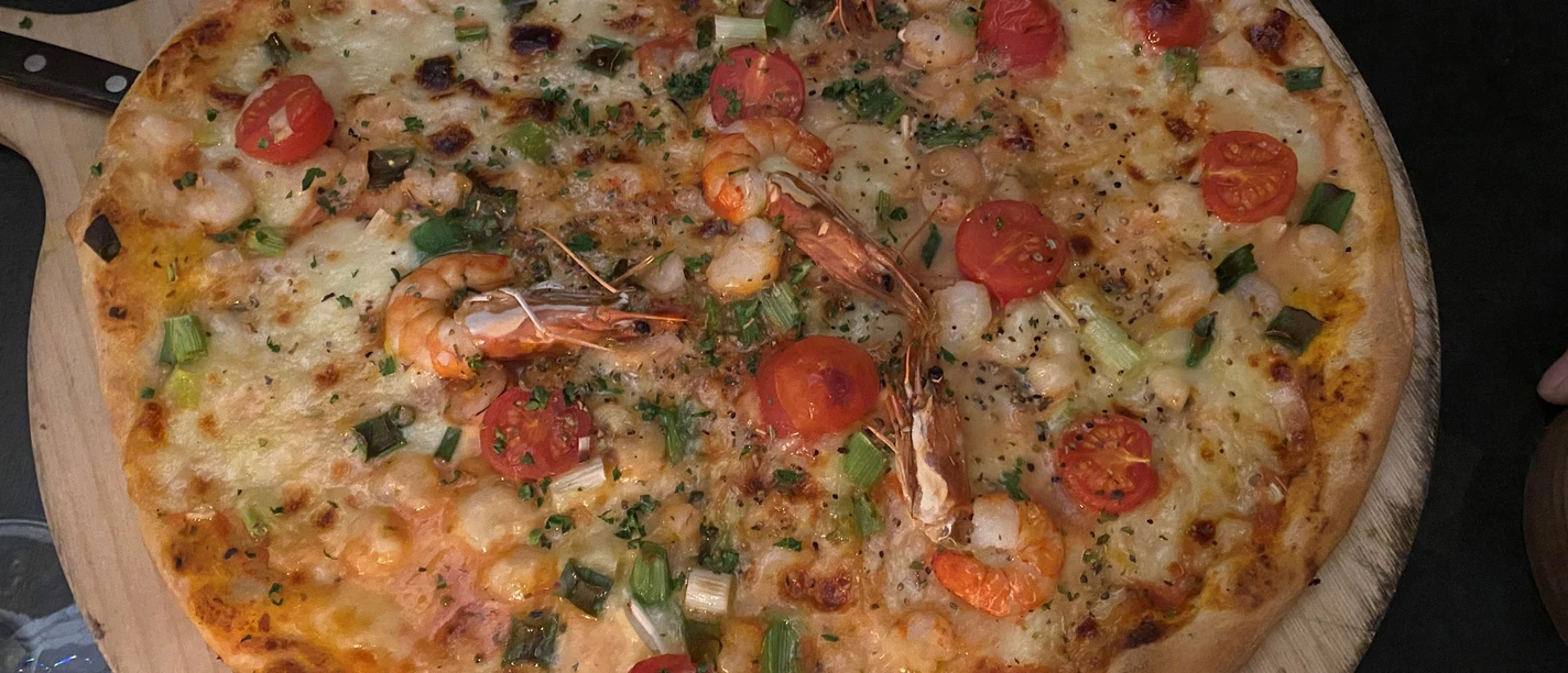 Vers gebakken pizza met sappige garnalen, kerstomaatjes en lente-uitjes op een houten tafel.