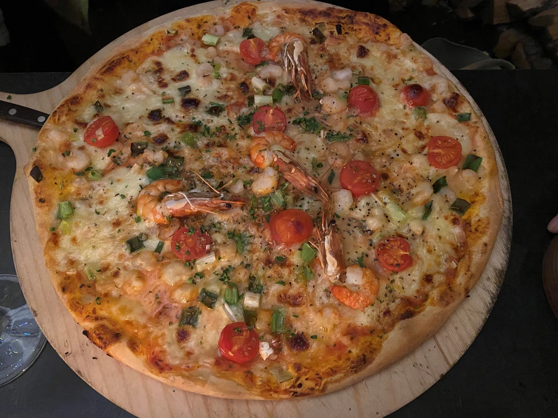 Pizza Frisch gebackene Pizza mit saftigen Garnelen, Kirschtomaten und Frühlingszwiebeln auf einem Holztisch.