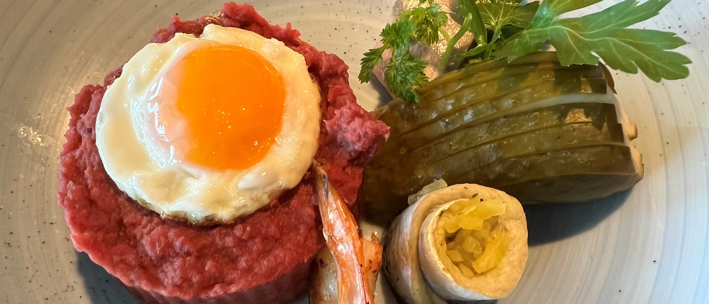 Labskaus with fried egg, gherkin and rollmops on a ceramic plate, appetizingly served.