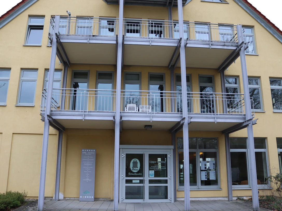 IMG_0475.JPG Blick auf den Eingang eines modernen, mehrstöckigen Gebäudes mit Balkonen und großen Fenstern.