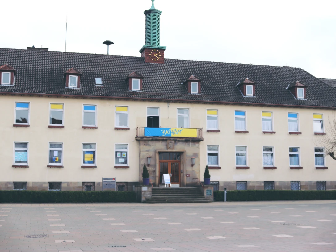 Kommunalgebäude mit gelb-blauen Flaggen über dem Eingang, großer leerer Platz im Vordergrund.