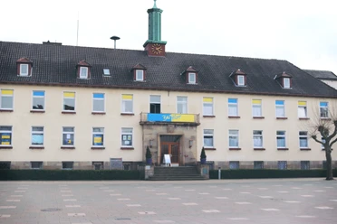 IMG_0065.JPG Kommunalgebäude mit gelb-blauen Flaggen über dem Eingang, großer leerer Platz im Vordergrund.