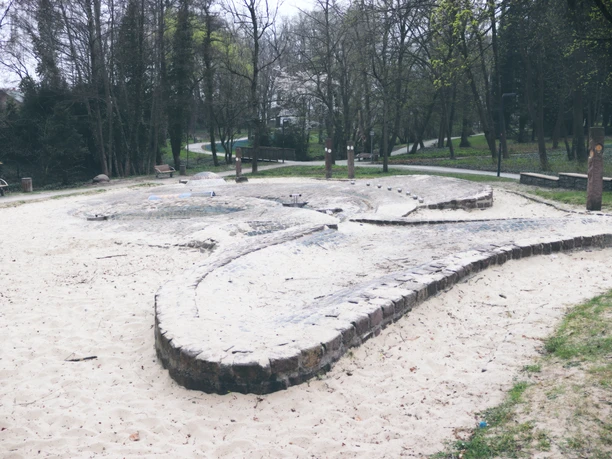 IMG_0430.JPG Ein weitläufiger Sandplatz im Park mit niedrigen gemauerten Strukturen unter kahlen Bäumen.